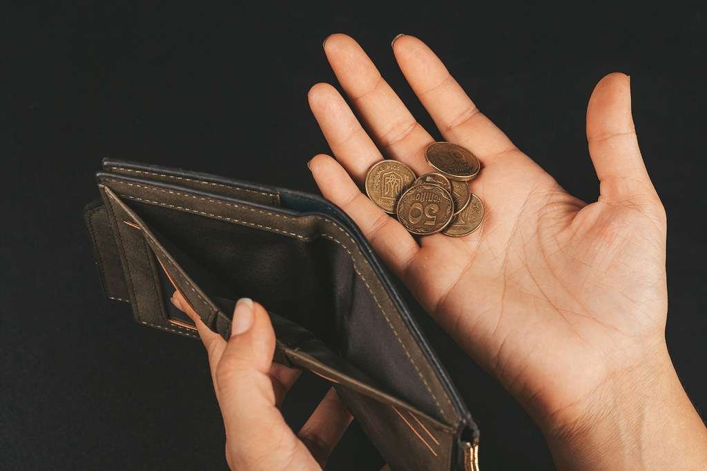 man holding empty wallet in one hand and some coins on other hand