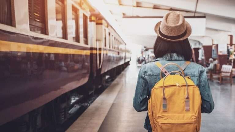 a girl with yellow bag and brown hat standing at the train station